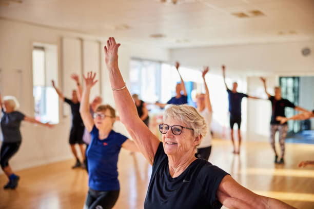 Une femme âgée souriante, en tenue de sport, participant à un cours de gymnastique avec d'autres seniors